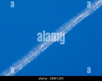 White condensation trail from an airplane flying at high altitude in a blue clear cloudless sky. Trace of water vapor and ice crystals. Stock Photo