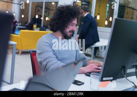 Young man working on his computer in co-creative space.  Working on new creative digital projects inside modern co working space. Stock Photo
