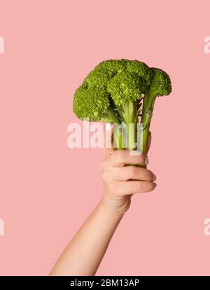 Eat green. Female hand showing broccoli on pink background, close up Stock Photo