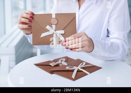 close-up photo of gift certificate, card, wedding invitation card. female hands holding a bronze invitation envelope with a wax seal