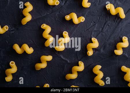 Scattered cavatappi uncooked golden wheat curly pasta pattern on textured dark black background, top view Stock Photo