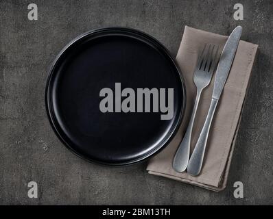 Black empty plate, cutlery and napkin on gray concrete background. Top view Stock Photo