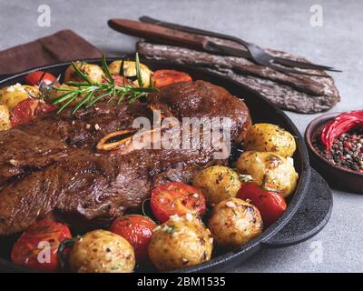 grilled beef steak with bone, roasted new potatoes  tomato with garlic in a pan Stock Photo