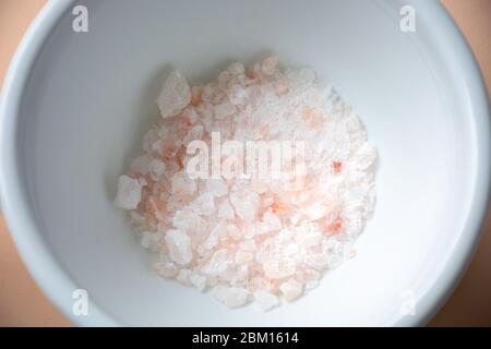 Crushed himalayan pink rock salt pieces crystals in a ceramic white bowl mortar Stock Photo