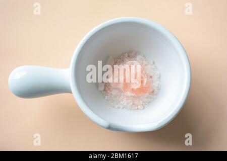 Himalayan pink rock salt crystals pieces in a ceramic white bowl mortar on coral background Stock Photo