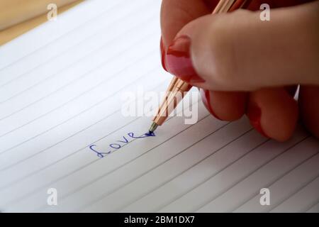 Close up manicured female hand writes the word love in notebook. Valentine's day and love concept. Stock Photo