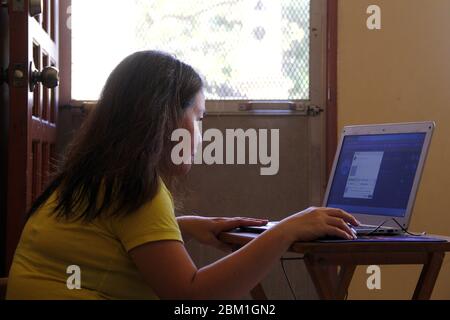 Photo of an Asian woman working on a computer in the living room of her house Stock Photo