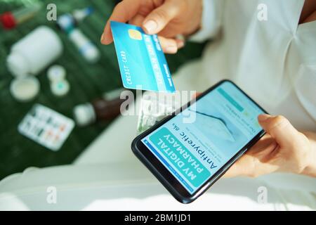 Closeup on woman with credit card and empty blister pack of pills buying pharmacy on internet using smartphone at home in sunny day. Stock Photo