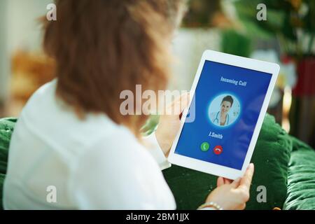 Seen from behind woman at home in sunny day having incoming call from doctor. Stock Photo