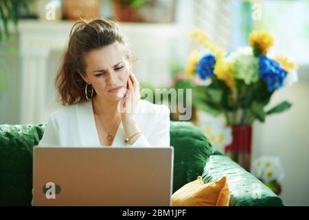 stylish middle age housewife in white blouse with toothache speaking with dentist using telehealth technology in the modern house in sunny day. Stock Photo