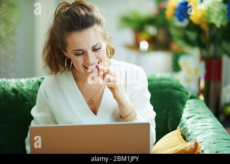 middle age housewife in white blouse speaking with dentist using tele health technology in the modern living room in sunny day. Stock Photo