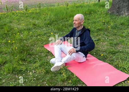Old men practicing in a yoga outdoor in the park on the yoga mat Stock Photo