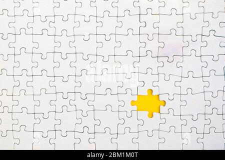 Yellow background showing through missing piece in white jigsaw puzzle. Stock Photo