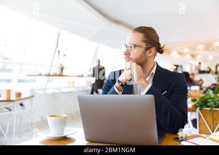 Image of handsome concentrated young businessman indoors in office using laptop computer. Stock Photo