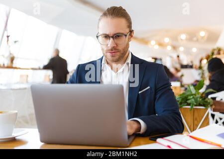 Image of handsome concentrated young businessman indoors in office using laptop computer. Stock Photo