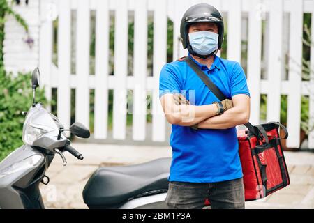 Portrait of happy confident delivery man standing at scooter with big cooler bag full of products Stock Photo