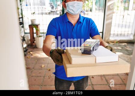 Positive delivery man holding stack of pizza boxes with payment terminal on top Stock Photo