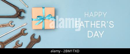Happy Father's day card with gift box tied with blue ribbon in polka dots and wrench on blue background. Banner for website. Stock Photo