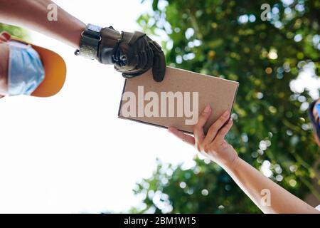Delivery man in medical mask giving small cardboard box to customer, view from below Stock Photo