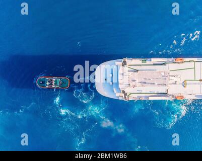 Tugboat towing large container ship blue sea port. Aerial top view