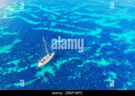 Pleasure yacht with sail stands on coral reef in blue transparent turquoise water sea caribbean. Concept travel. Aerial top view. Stock Photo