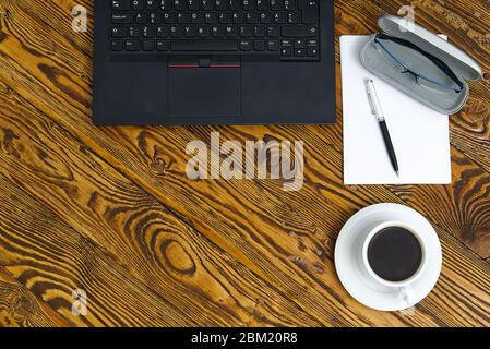 Laptop with cup of coffee on old brown wooden table. Top view to Notebook with cup of fresh coffee in home office in village. Stock Photo