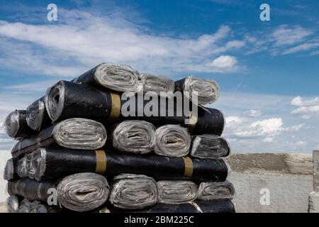 A close-up of rolls of new black roofing felt or bitumen that is precisely folded against a blue sky Stock Photo