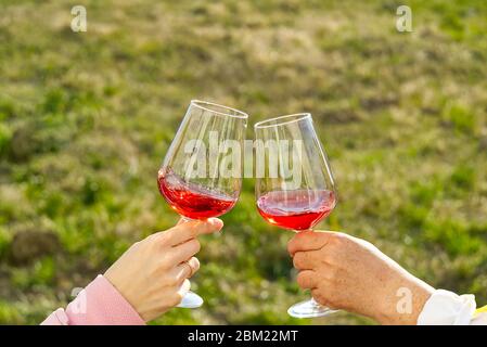 Clink with red wine glasses outside on the garden. garden party. Two people clinking each other's glasses with rose wine. Stock Photo