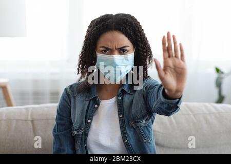 Angry african woman wearing medical face mask showing STOP gesture at home Stock Photo