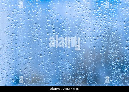 Close-up of water droplets on a light blue running down on glass transparent surface. rainy drops on a window pane during a summer shower stormy weath Stock Photo