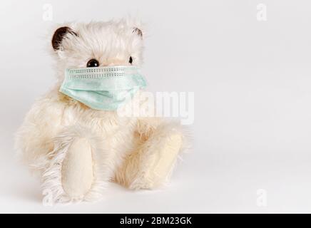 Teddy bear sitting in face medical mask on white background. Pediatrics and disease prevention concept. Copy space Stock Photo