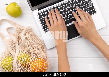 Food grocery online shopping delivery. Eco friendly natural bag with fruits and laptop on wooden table Stock Photo