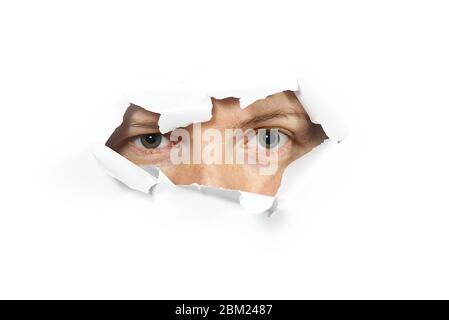 Young woman peeping through hole on paper. Female Eye looking through hole. Isolated on white background. Spy concept Stock Photo