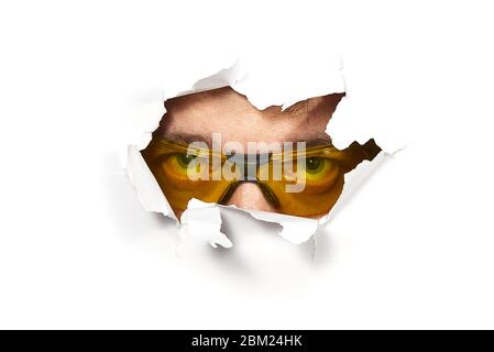 Man in shooting glasses peeping through hole on paper. Male in ellow glasses looking through hole. Isolated on white background. Spy concept Stock Photo