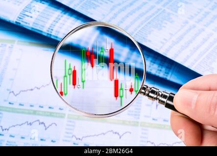 Magnifying glass shows a stock price as a candlestick chart. Price tables and charts are displayed in the background. Stock Photo