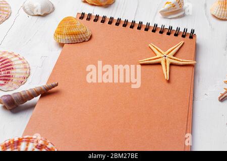 Brown open notepad surrounded by sea shells on white wooden table closeup Stock Photo