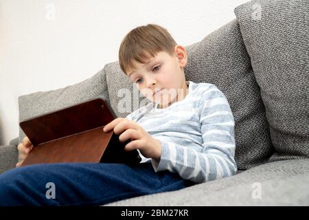 Distance learning online education. A schoolboy is studying using a tablet. A child sits on a sofa in a tablet Stock Photo