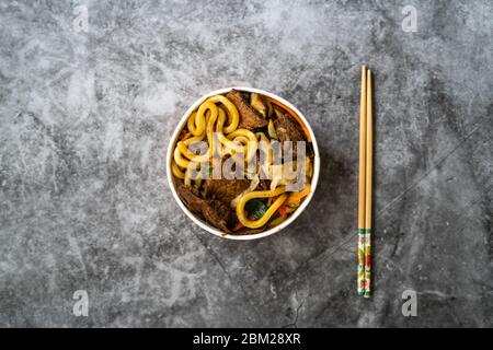 Take Away Asian Style Japanese Udon Noodle Soup with Beef, Mushroom and Vegetables in Plastic Bowl Package / Container. Traditional Fast Food. Ready t Stock Photo