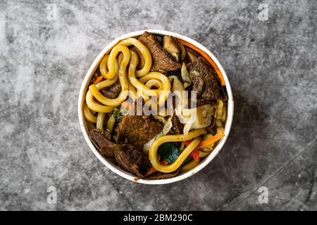 Take Away Asian Style Japanese Udon Noodle Soup with Beef, Mushroom and Vegetables in Plastic Bowl Package / Container. Traditional Fast Food. Ready t Stock Photo