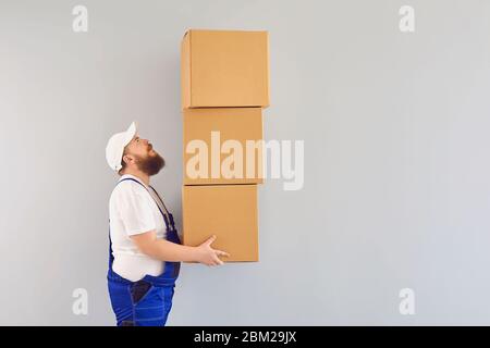 Funny fat bearded delivery courier loader man in a blue uniform with a cardboard box in his hands smiling on a gray background. Delivery of goods pack Stock Photo