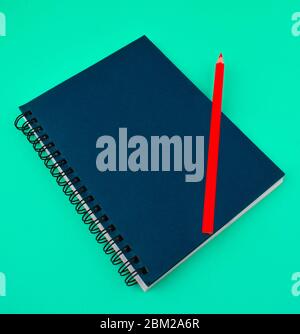 A red color wood pencil crayon placed on top of a single blue colored paper diary Stock Photo