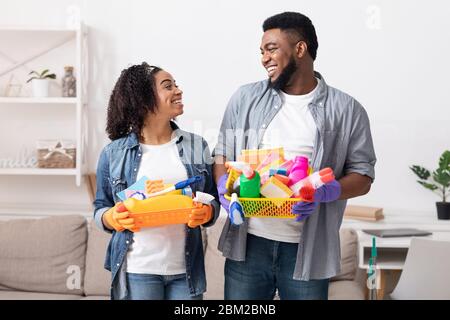 Big Cleaning Day. Smiling Black Couple Holding Containers With Household Tools Stock Photo