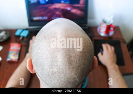 Rear view of a bald man playing a computer game. Stock Photo