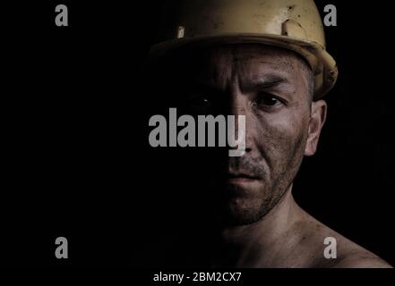 Miner in a yellow hard hat on a black background dirty with coal dust Stock Photo