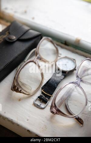 Old glasses and retro watch on white background near window Stock Photo