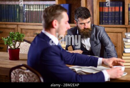 Men with serious faces in retro interior with bookshelves on background. Men in suits, oldfashioned professors, scientists in library with antique books, defocused. Professors and scientists concept. Stock Photo