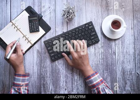 young man typing on keyboard while writing on notebook  Stock Photo