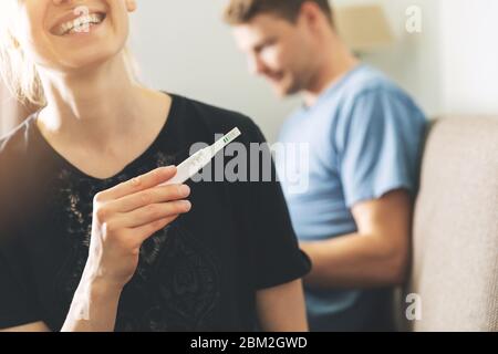 young happy woman sitting on couch at home and holding positive pregnancy test Stock Photo