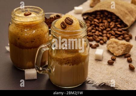 Dalgona coffee in mason jar. Korean fluffy whipped coffee beverage. Trendy quarantine drink, sugar and coffee beans on black stone concrete background Stock Photo