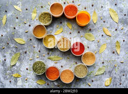 Variety of colorful dried herbs and spices in cups. S shape. Selection of herbs and spices on grey background. Cooking, eating concept. Top view. Stock Photo